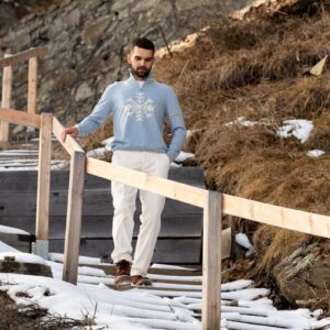 Herr trägt hellblauen Fedeli Cashmere Zip Polo mit Schneeflocken-Intarsia auf einem winterlichen Holzsteg in den Bergen.